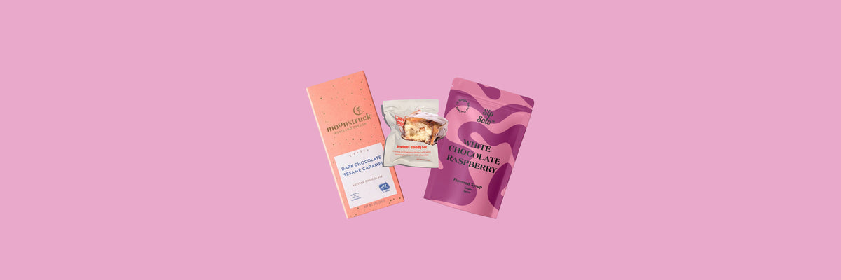 Peach chocolate bar, pretzel candy bar and pink syrup pouch on a pink background