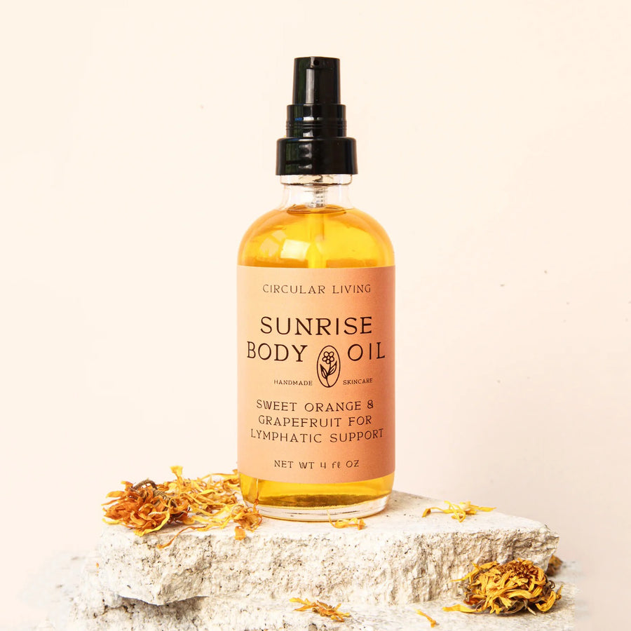 Circular Living Sunrise Body Oil in an amber bottle on a stone pedestal with dried orange flowers, on cream.
