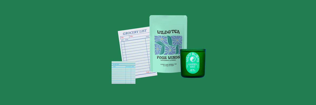 Two notepads, a mint-green tea pouch and a green glass candle on a deep green background