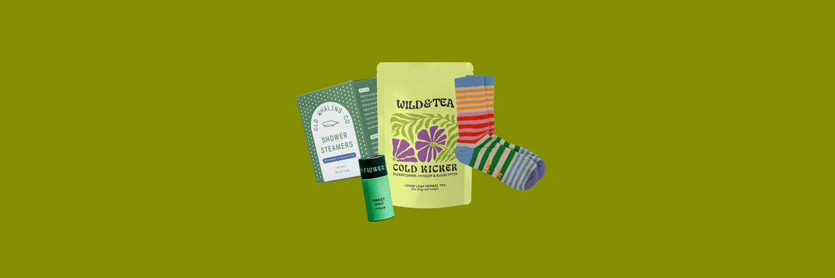 Shower steamers box, lip balm tube, yellow-green tea pouch and striped socks on an olive green background