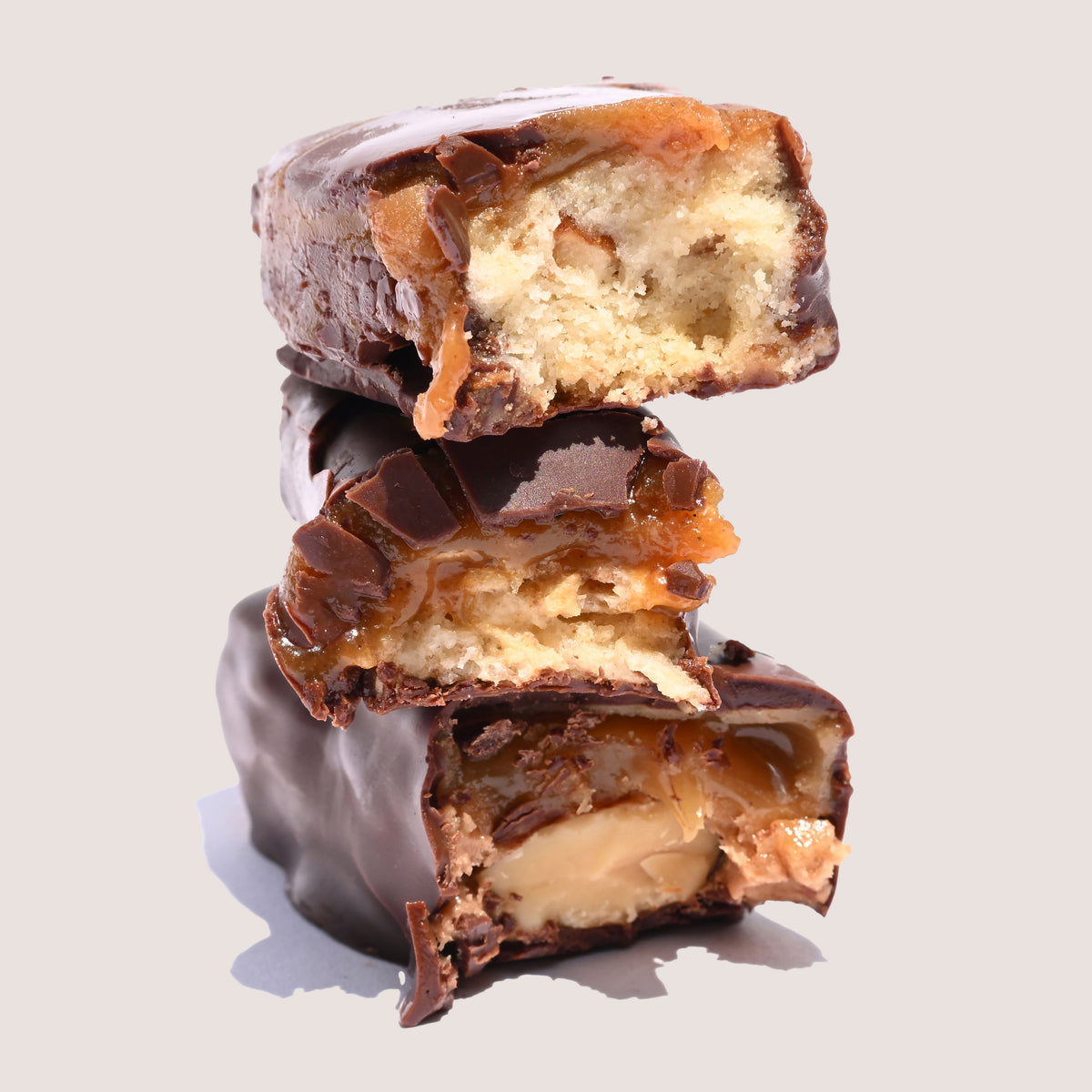 Three stacked chocolate-covered candy bars with a creamy filling, shown cut open on a light gray background.