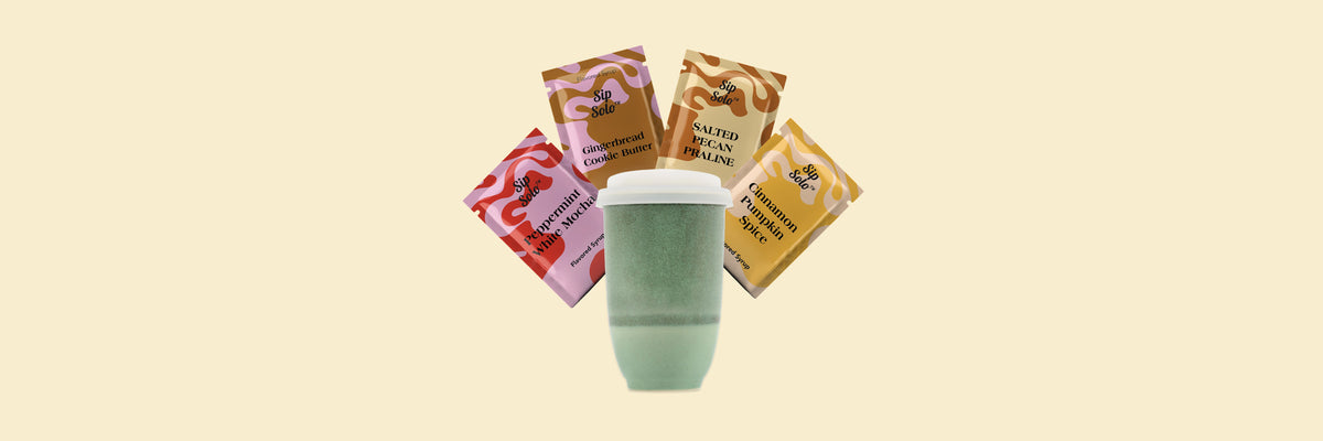 Four flavored syrup packets and a green ceramic travel cup with a lid on a cream background