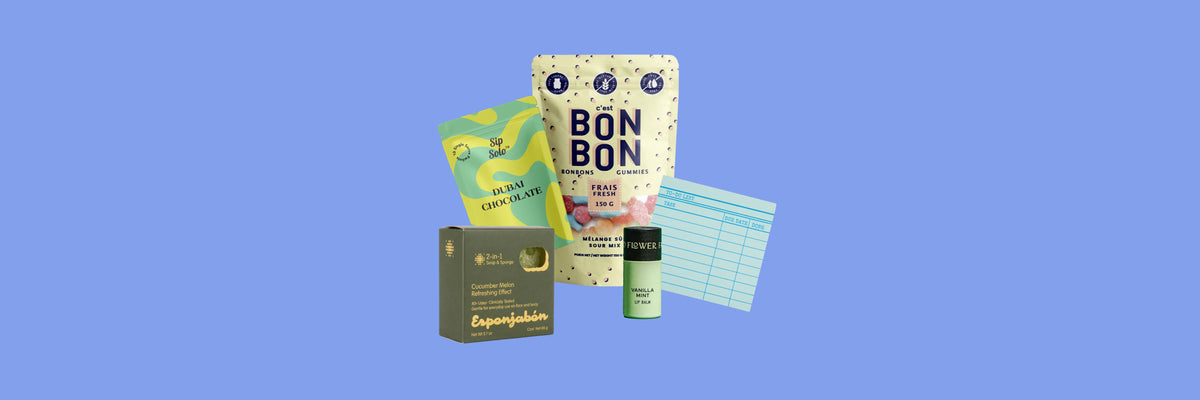 Syrup pouch, gummy candy bag, soap and sponge box, lip balm and a notepad on a periwinkle blue background