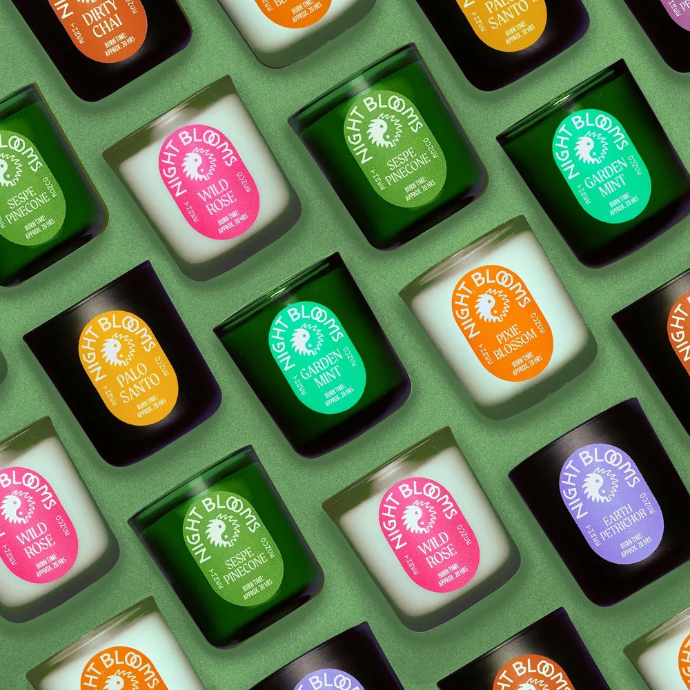 A repeating flat-lay arrangement of Night Blooms scented candles in glass jars with black lids and colorful labels, set against a sage green background.