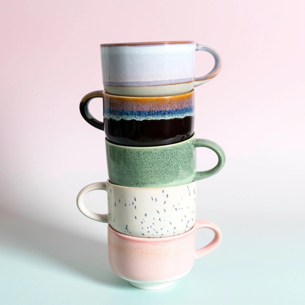 Stack of ceramic mugs in pastel and earthy colors against a pink and mint background.