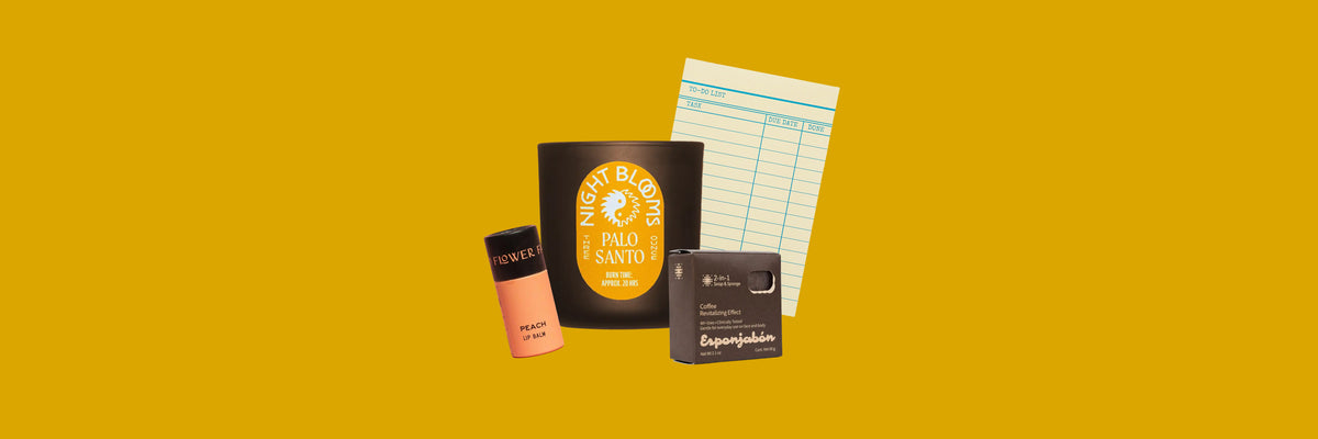 Peach lip balm, black glass candle, brown soap and sponge box and a to-do notepad on a mustard yellow background