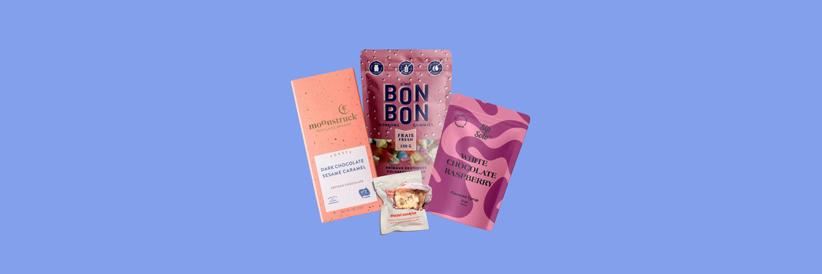 Peach chocolate bar, gummy candy bag, candy bar and pink syrup pouch on a periwinkle blue background