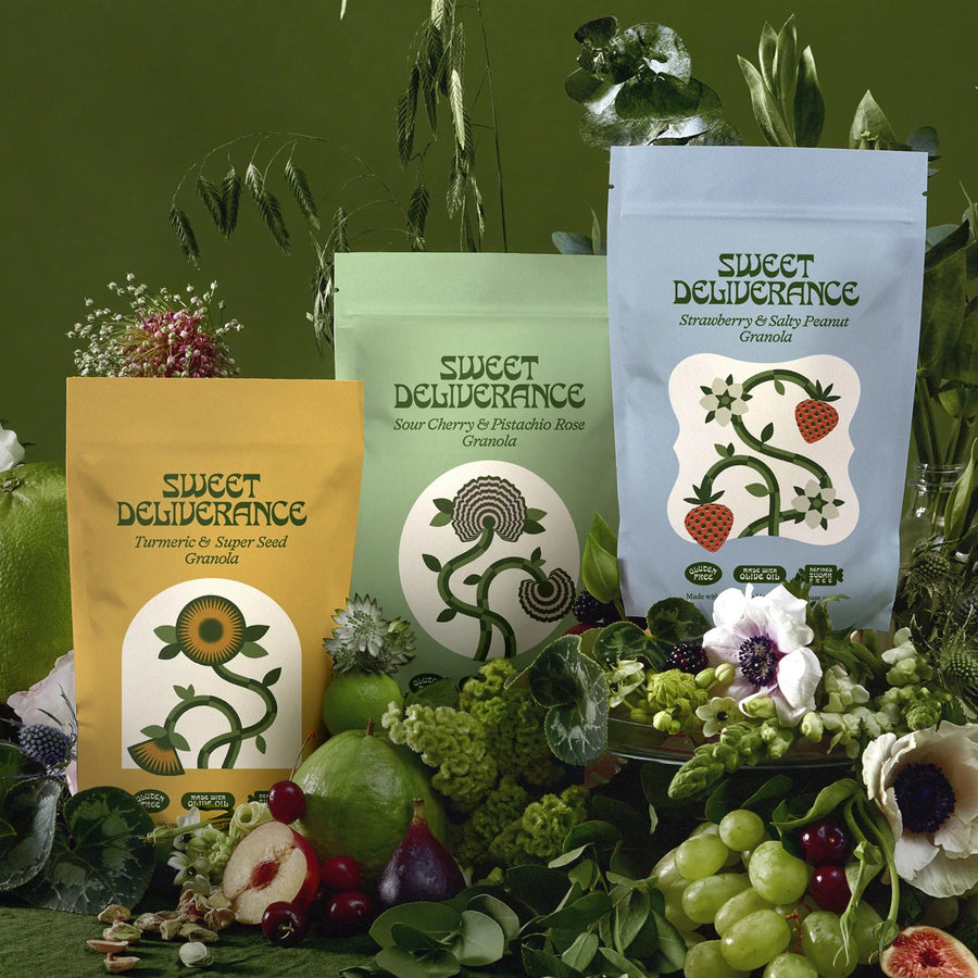 Three Sweet Deliverance granola pouches in yellow, light green and light blue, with fresh fruit and flowers on dark green.